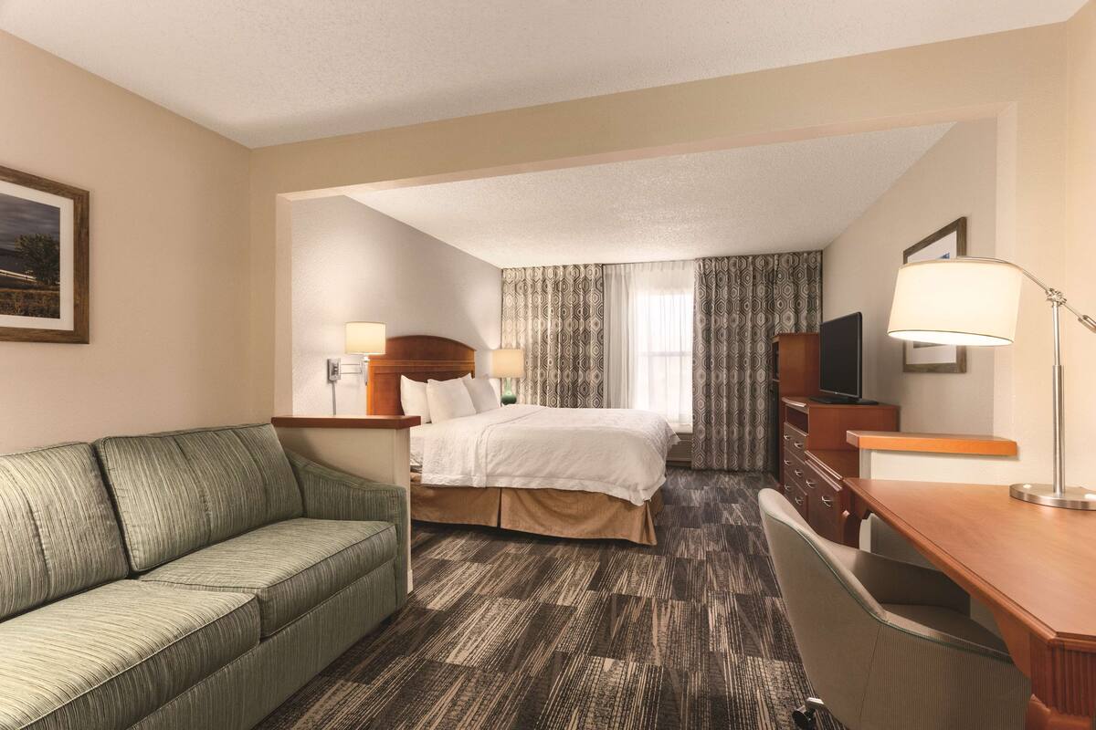 A hotel room with a bed, a desk, a chair, a sofa, and a TV.