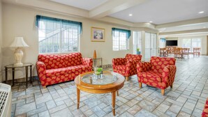 A spacious living room with red patterned sofas, a glass coffee table, and a dining area in the background.