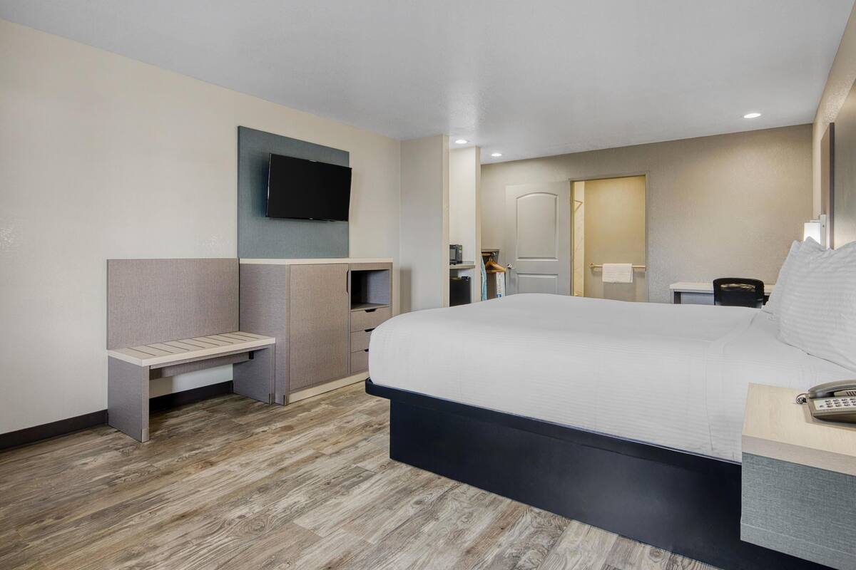 Een moderne hotelkamer met een groot bed, een bureau met telefoon, een aan de muur bevestigde televisie en een bankje.
