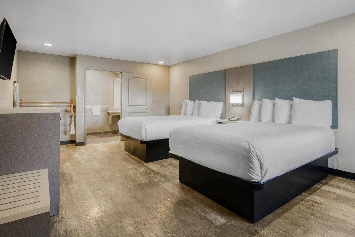 A hotel room with two beds, a desk, a mirror, and a bathroom door.