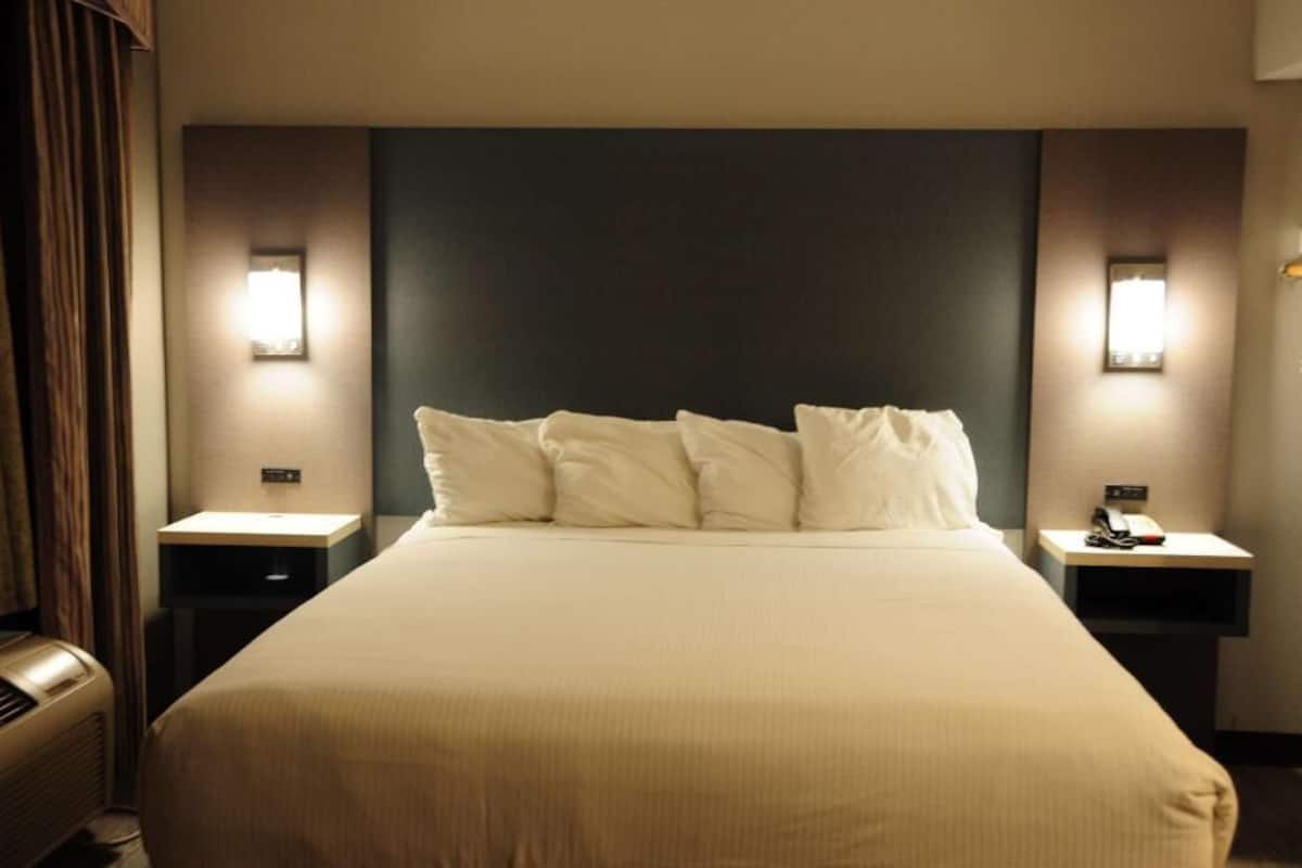 Een hotelkamer met een groot bed, twee nachtkastjes met lampen, een wandradiator en een donker hoofdeinde.