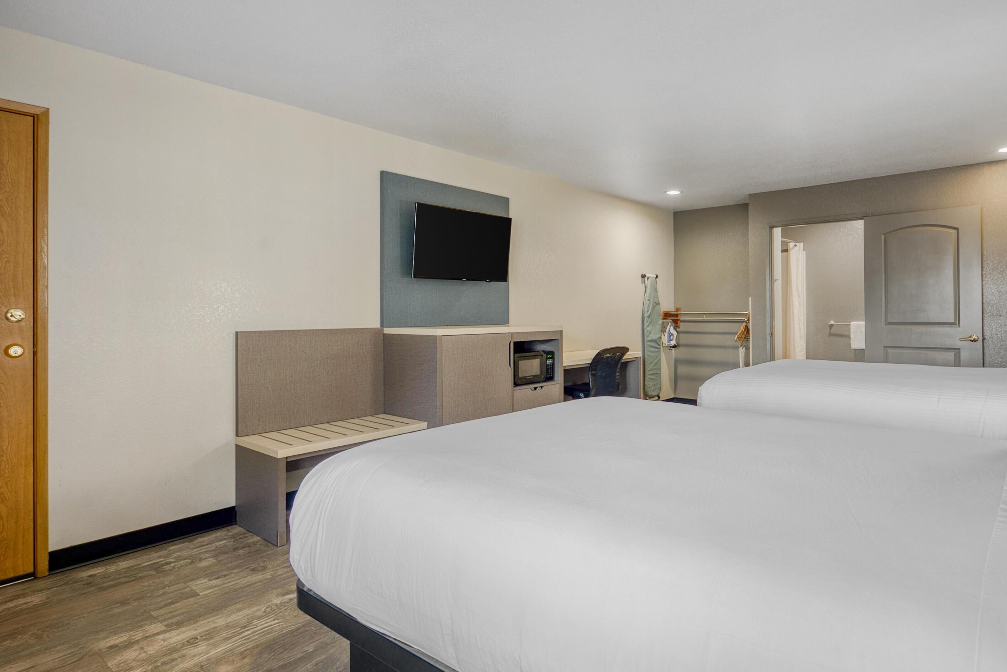 A hotel room with two beds, a TV mounted on the wall, a microwave, and a small desk.