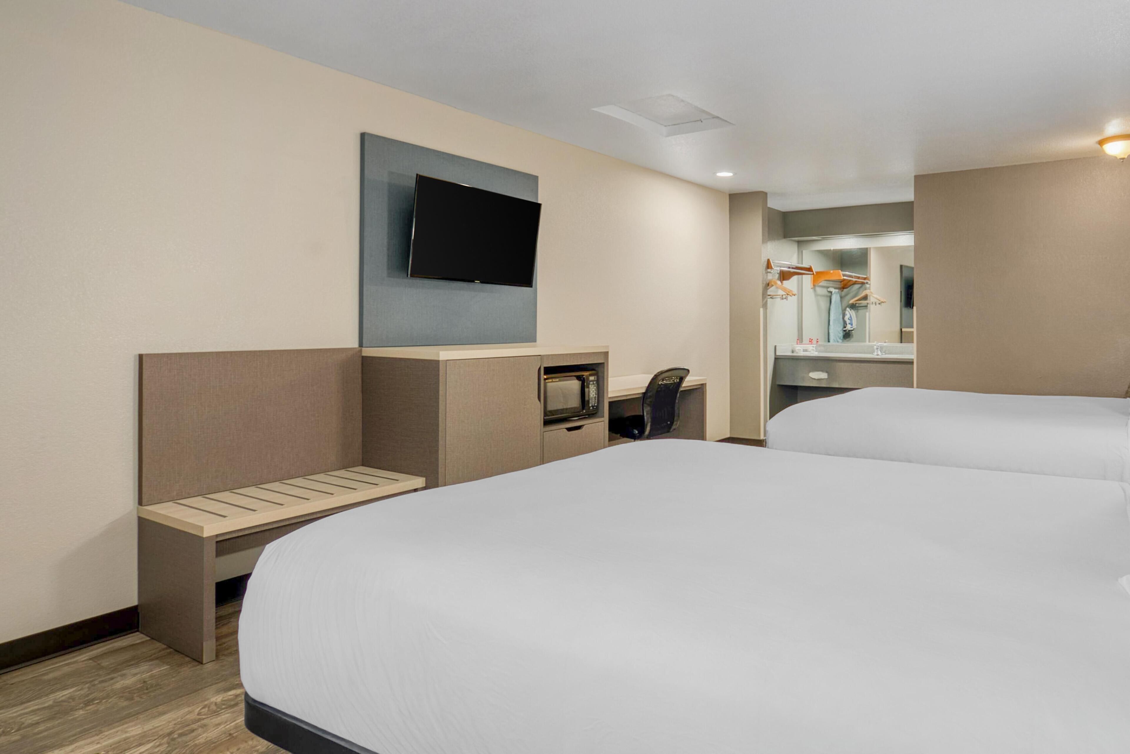 A hotel room with two beds, a flat-screen TV mounted on the wall, a microwave, and a small desk with a chair.