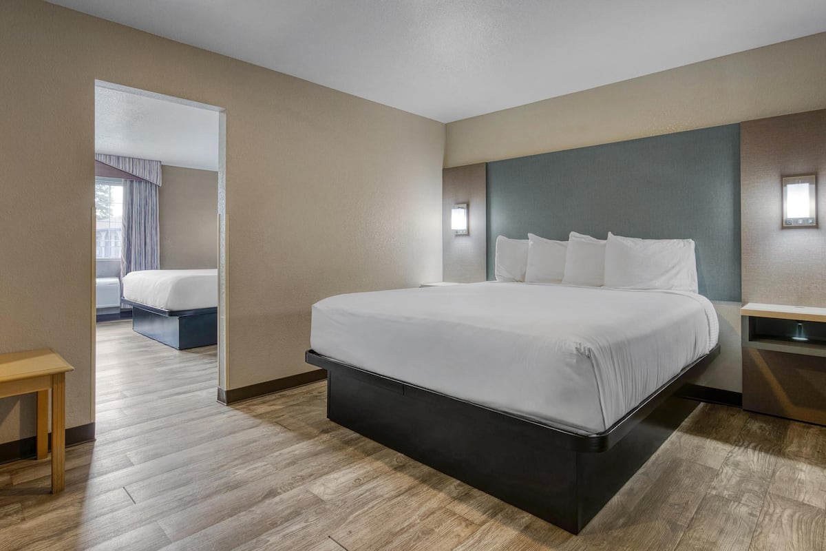 Een moderne hotelkamer met een groot bed, nachtkastjes en uitzicht op een andere kamer.