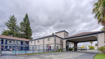 A motel with a swimming pool, covered parking, and a large building with a clock tower.