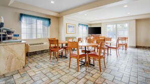 A dining area with multiple tables and chairs, a kitchen counter with appliances, and a television on the wall.