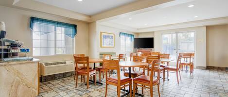 A dining area with multiple tables and chairs, a kitchen counter with appliances, and a television on the wall.