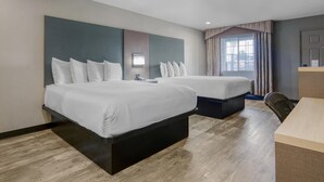 A hotel room with two beds, a desk, and a window with curtains.