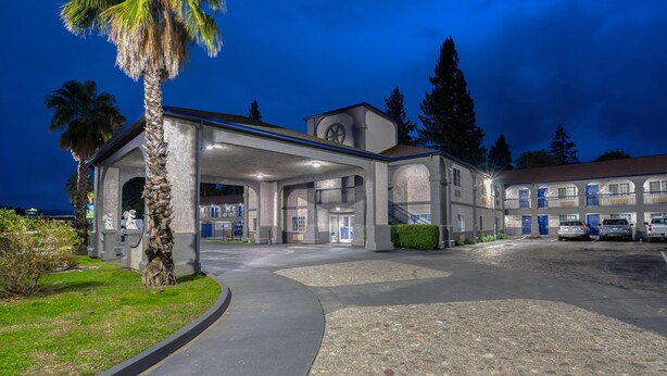 A hotel with a covered entrance, palm trees, and a parking area.