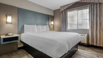 A modern hotel room with a large bed, bedside tables, and a window with curtains.