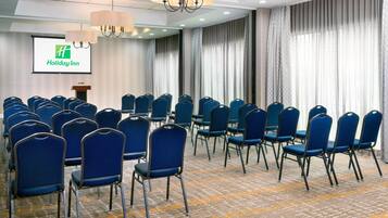 Une salle de conférence avec des rangées de chaises bleues, un pupitre et un écran affichant le logo de Holiday Inn.