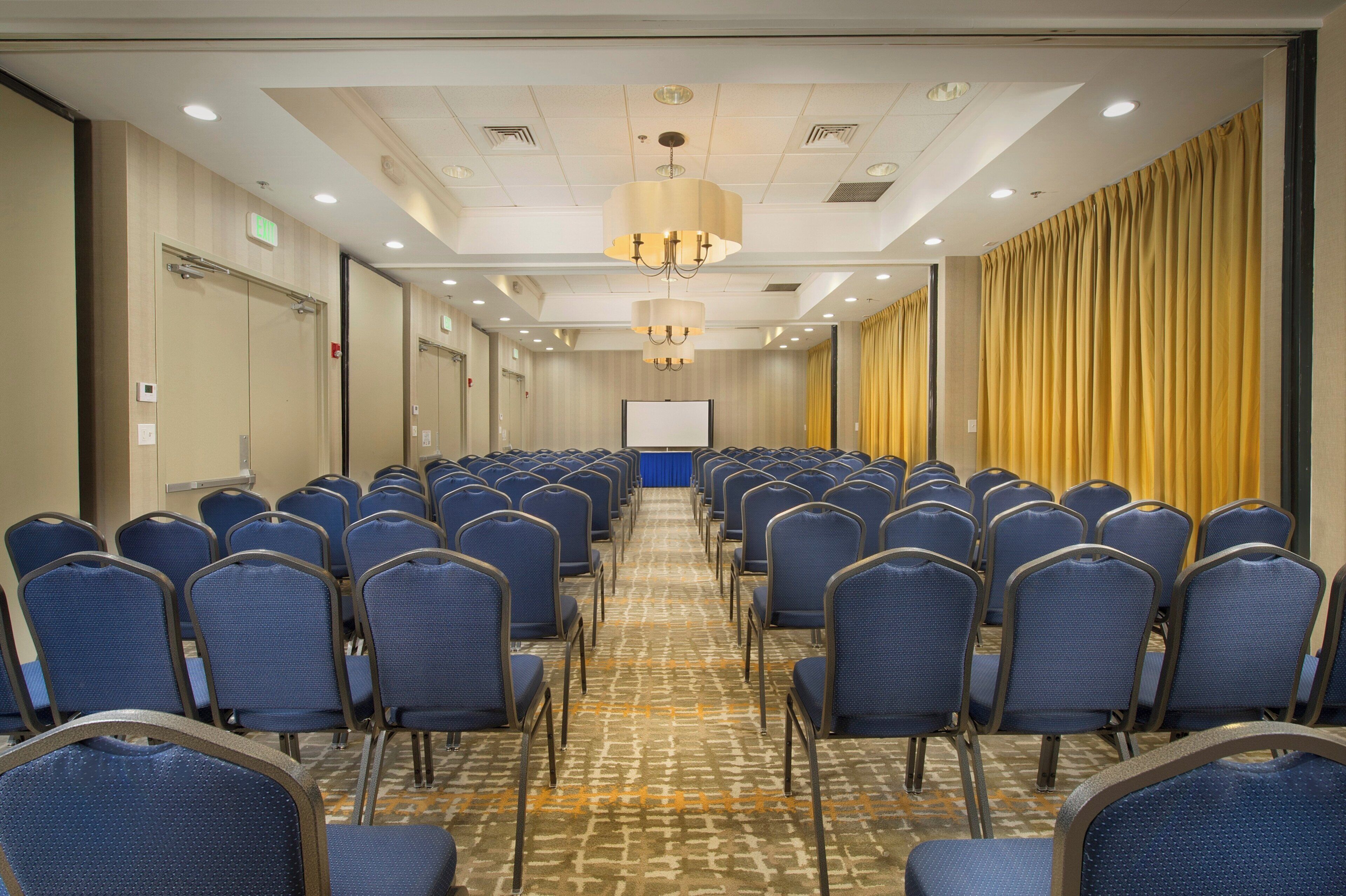 A conference room with rows of blue chairs, a whiteboard, and a patterned carpet.
