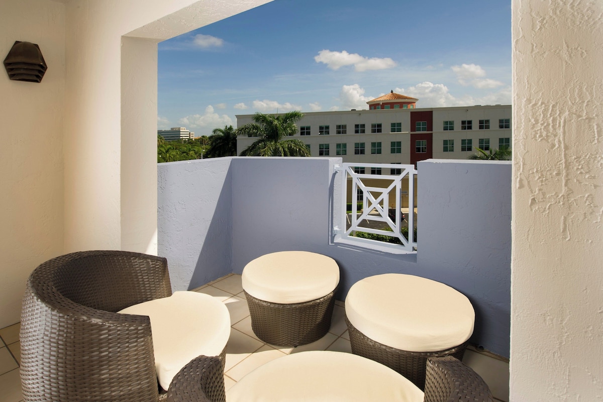 A balcony with wicker furniture and a view of a building with palm trees.