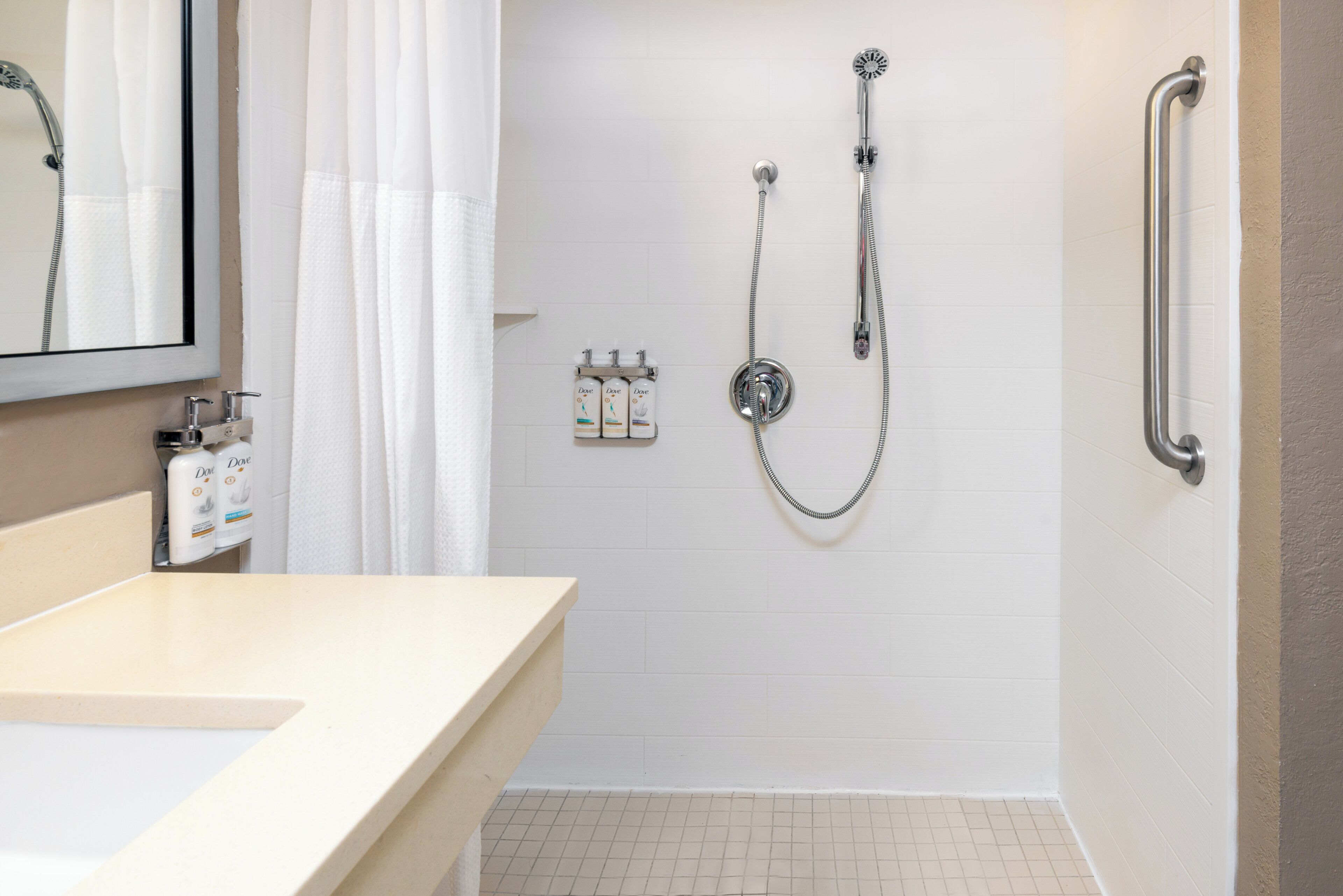 A bathroom with a shower, a handrail, a sink, and toiletries.