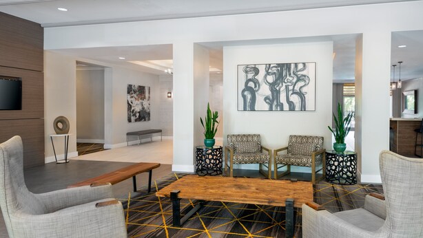 Et moderne loungeområde med et træbord, to grå polstrede lænestole, en stribet sofa og abstrakt vægkunst.
