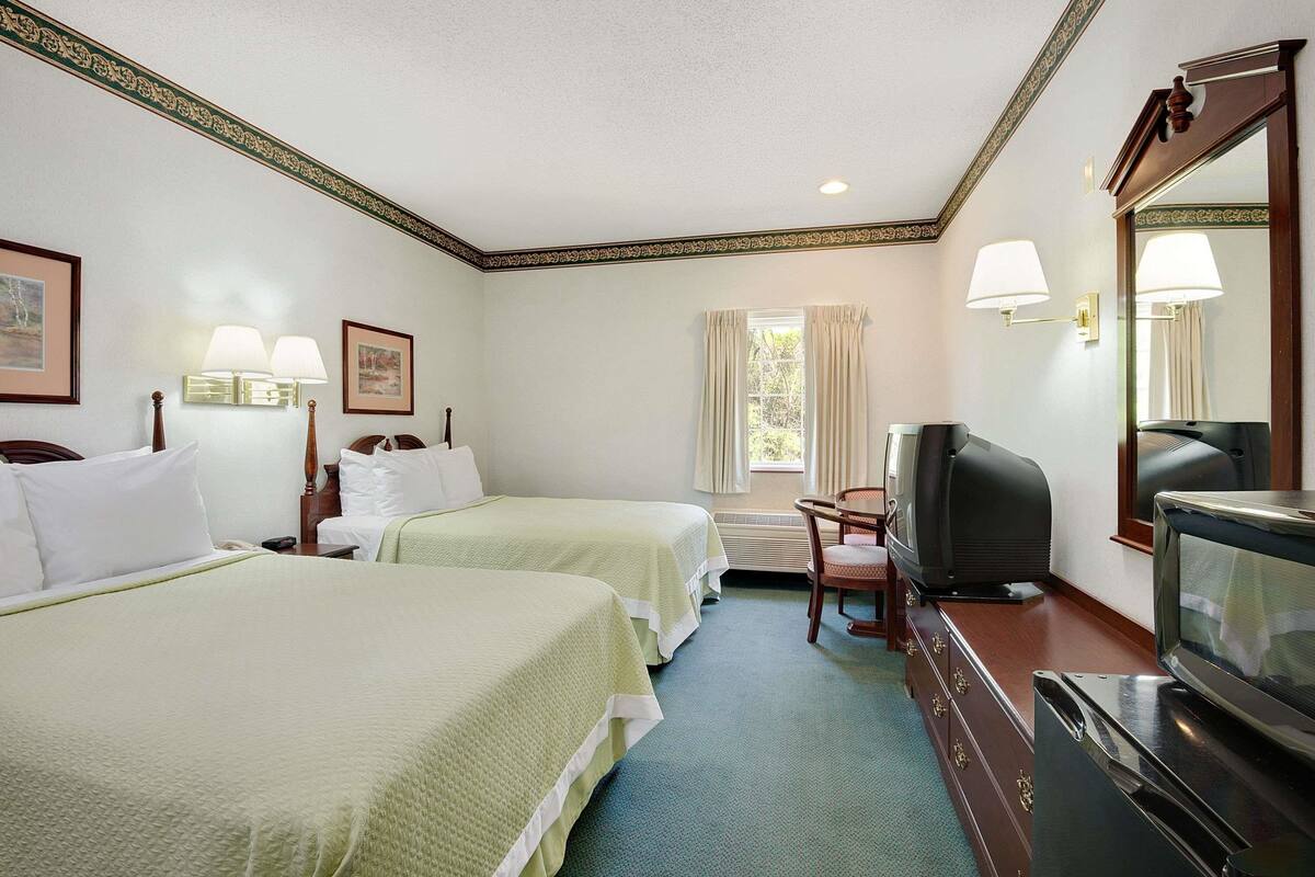 A hotel room with two beds, a television, a dresser, and a window with curtains.
