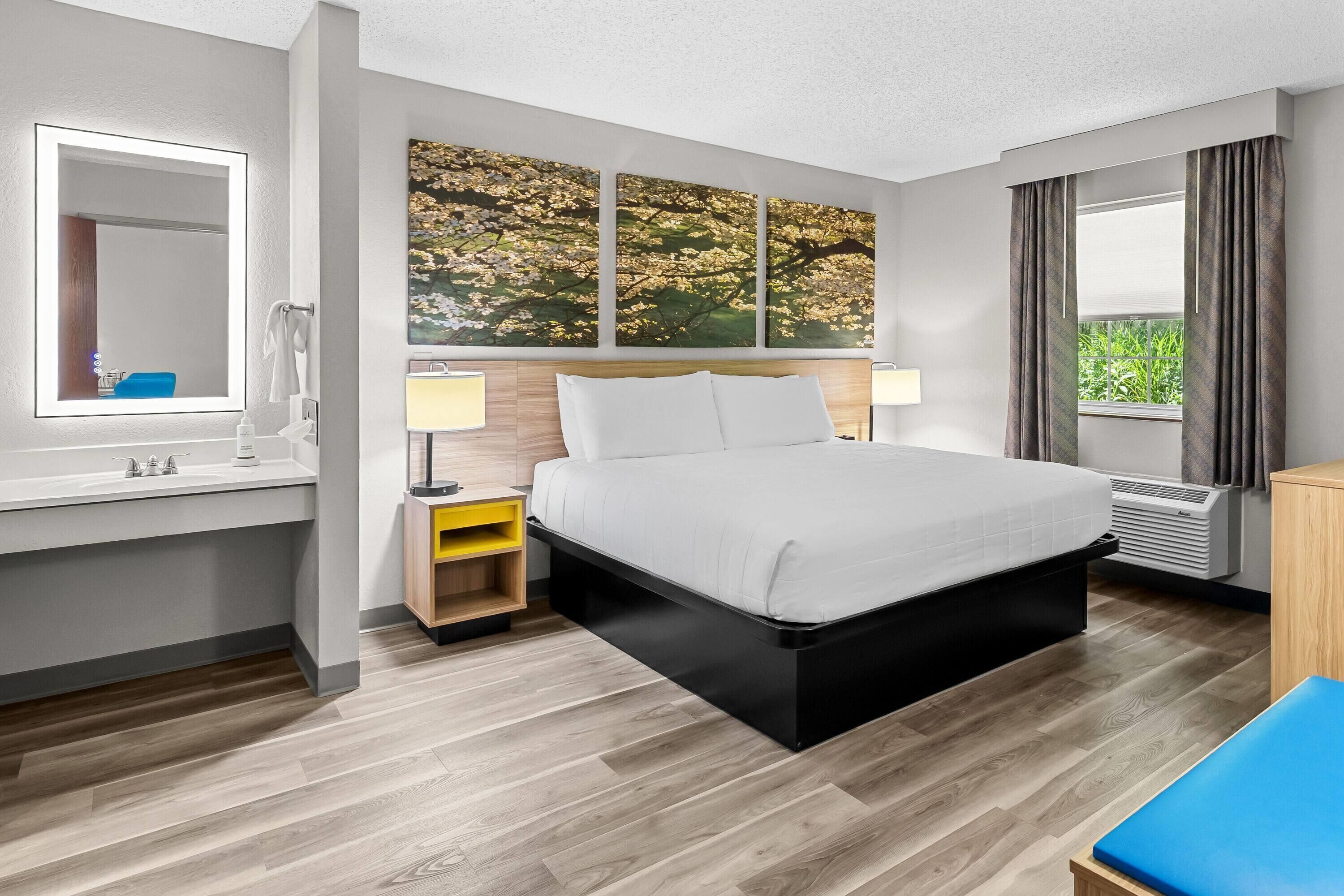 A hotel room with a bed, bedside tables, a mirror, and a window with curtains.