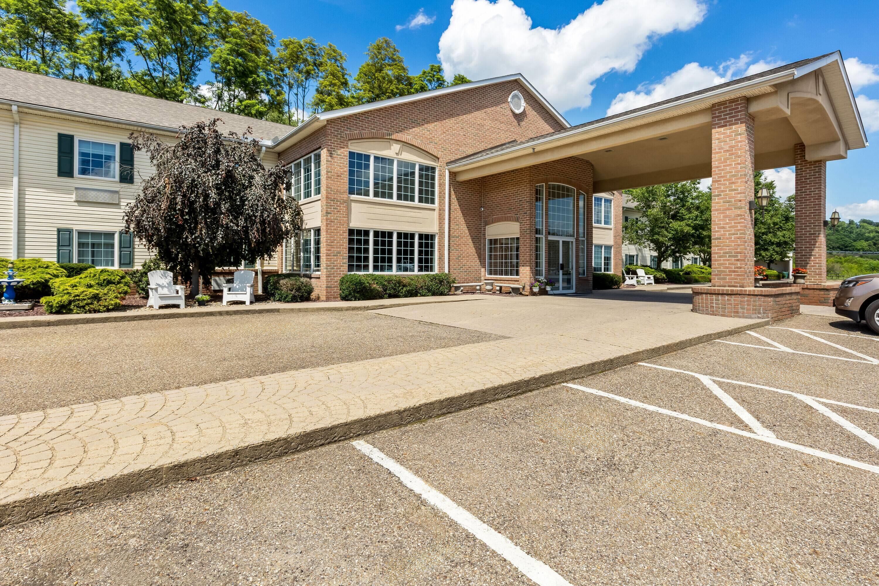A building with a covered entrance, a parking lot, and a tree in front.