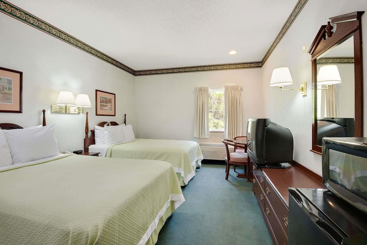 A hotel room with two beds, a television, a desk, and a window with curtains.