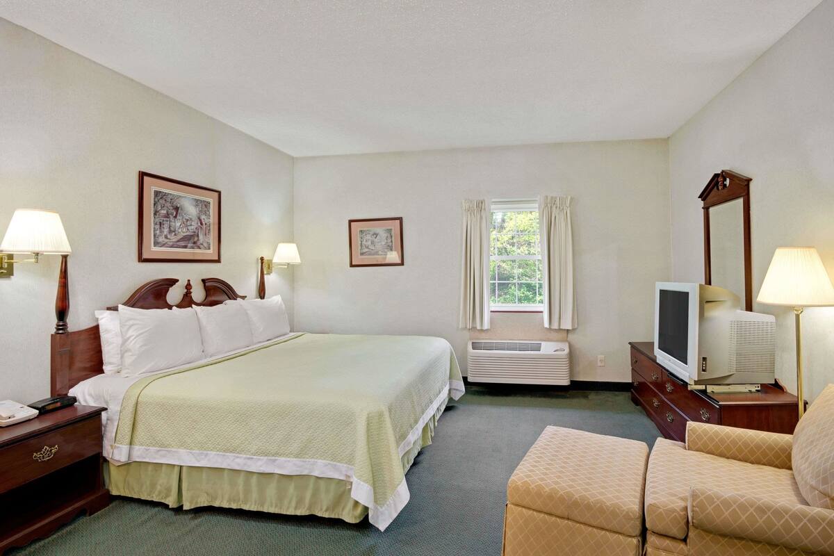 A hotel room with a bed, a television, a chair, and a window with curtains.
