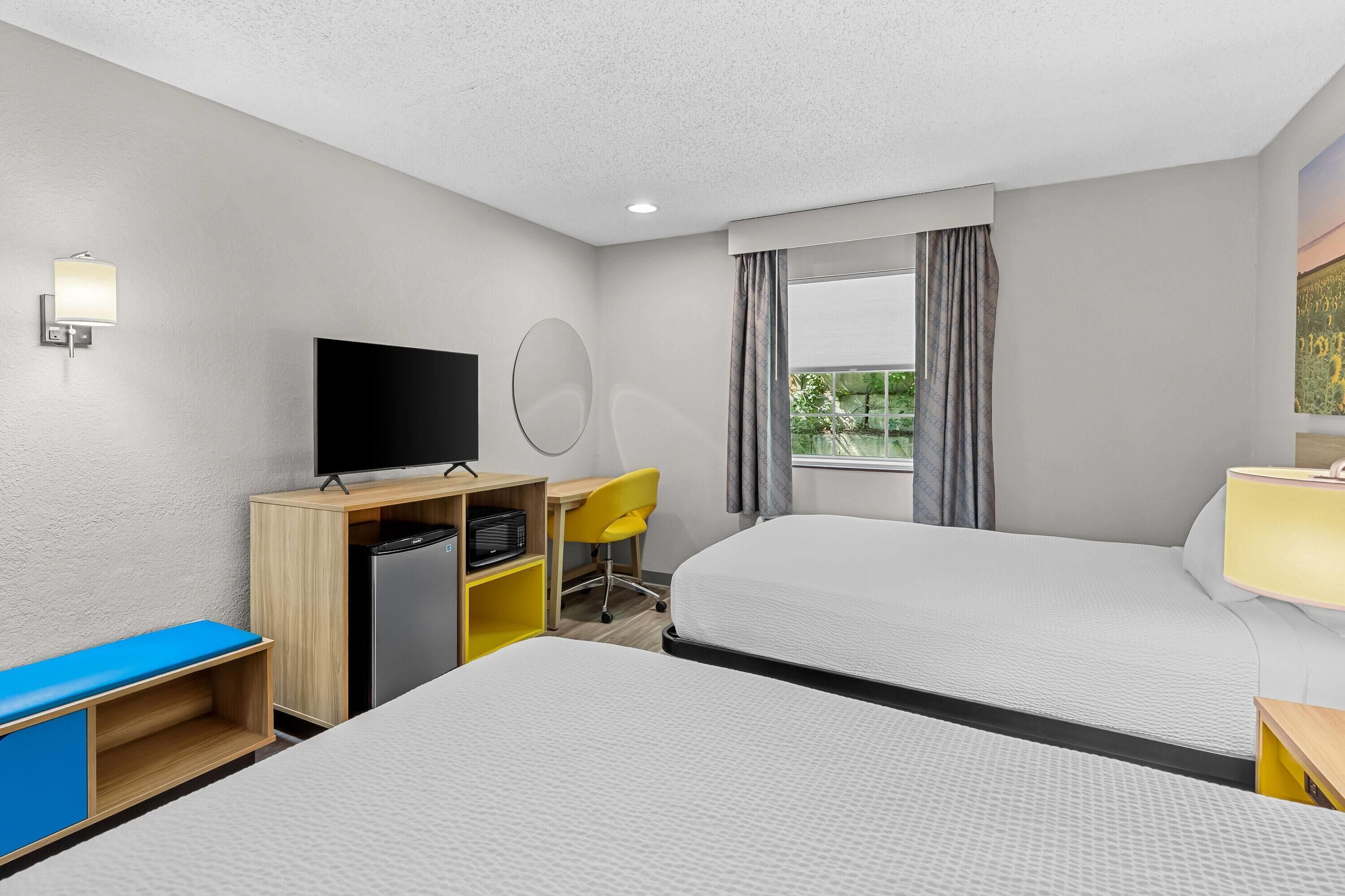 A hotel room with two beds, a desk with a television, a microwave, and a chair.