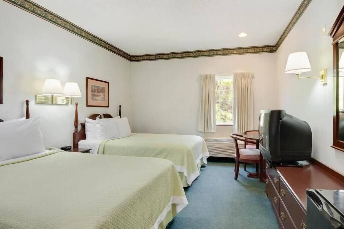 A hotel room with two beds, a television, a desk, and a chair.