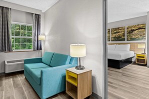 A hotel room with a sofa, a bedside table with a lamp, a bed, and a window with curtains. - Days Inn by Wyndham Lisbon (Lisbon)