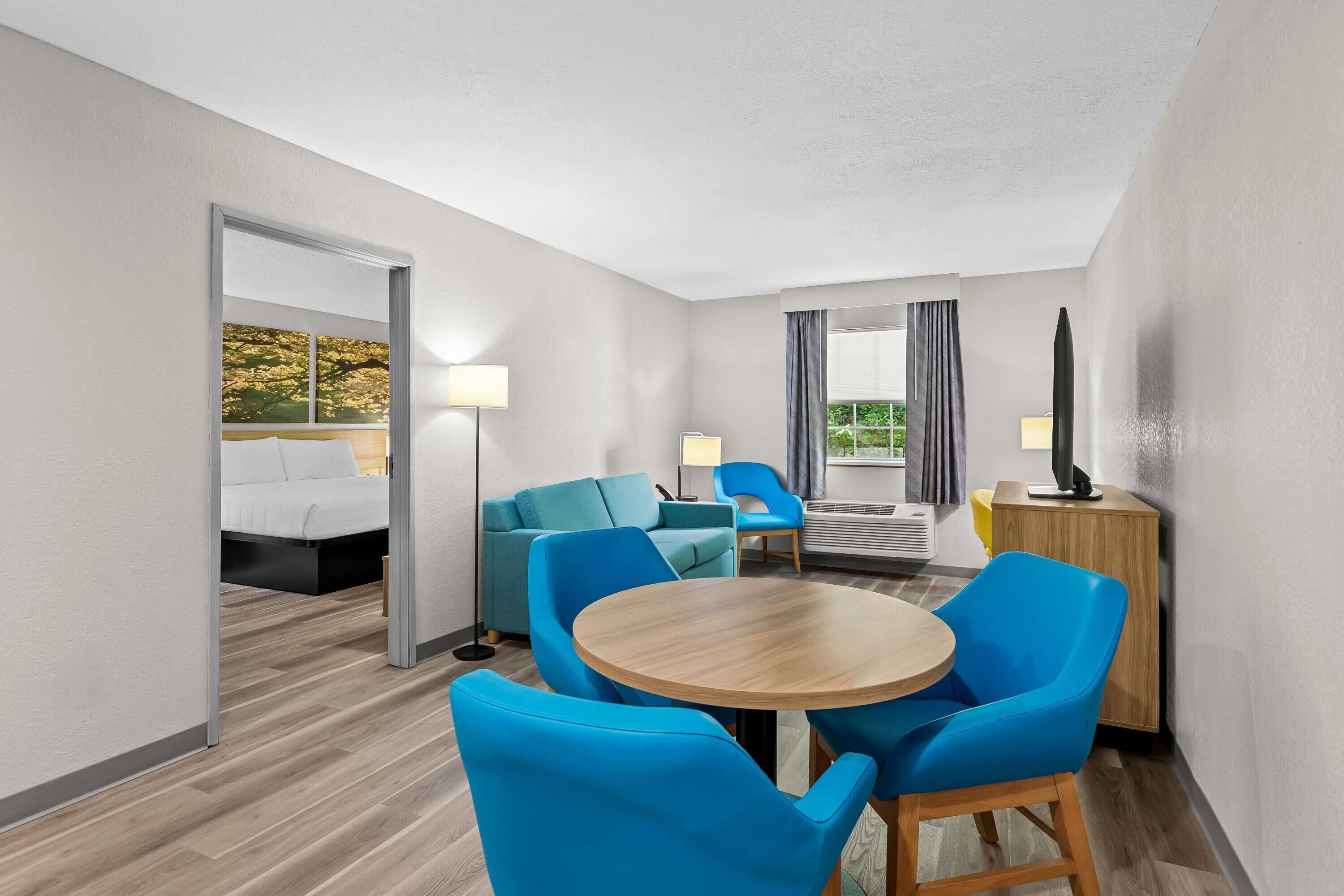 Habitación de hotel con cama, escritorio, silla, mesa redonda y vistas a árboles desde la ventana.