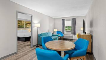 Habitación de hotel con cama, escritorio, silla, mesa redonda y vistas a árboles desde la ventana.