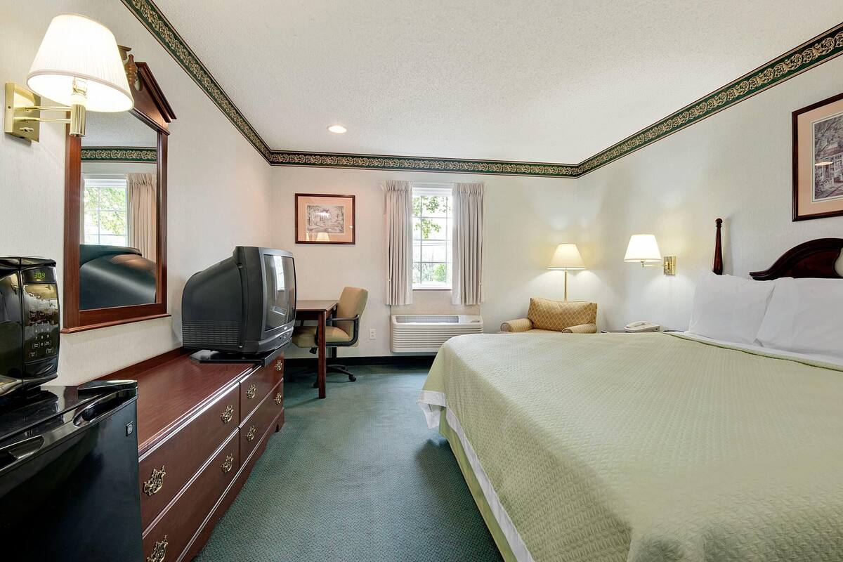 A hotel room with a bed, a desk with a television, a dresser, and a window with curtains.