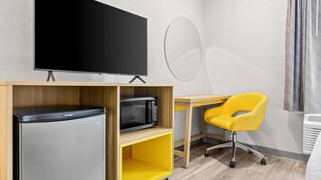 A room with a flat-screen TV, a microwave, a yellow chair, and a wooden desk.