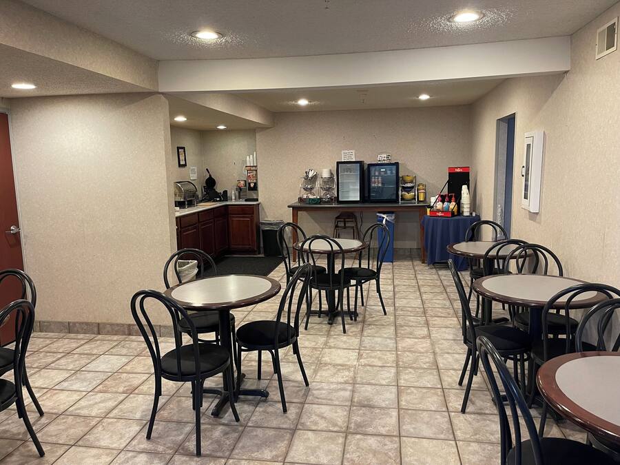 Ein Hotel-Essbereich mit mehreren Tischen und Stühlen, einer Küchenzeile und einem Kühlschrank.