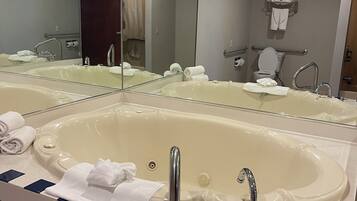 A bathroom with a large bathtub, a sink, a mirror, and a toilet.