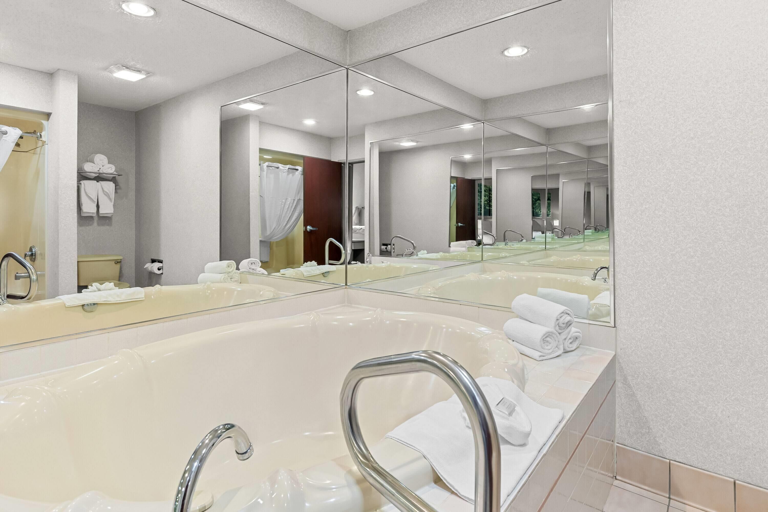 Un baño moderno con una bañera grande, varios espejos y toallas ordenadas.