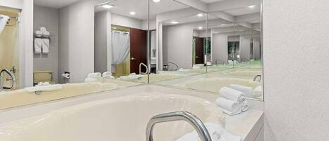 Un baño moderno con una bañera grande, varios espejos y toallas ordenadas.