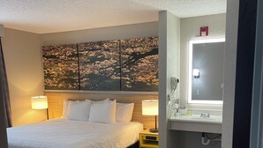 A hotel room with a bed, bedside lamps, a bathroom with a mirror, and a wall with a cherry blossom painting. - Days Inn by Wyndham Lisbon (Lisbon)