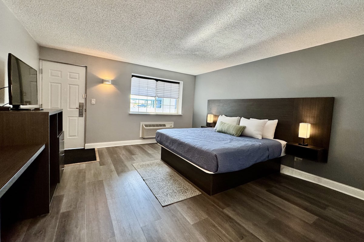 A bedroom with a bed, a TV, a window, and a door.