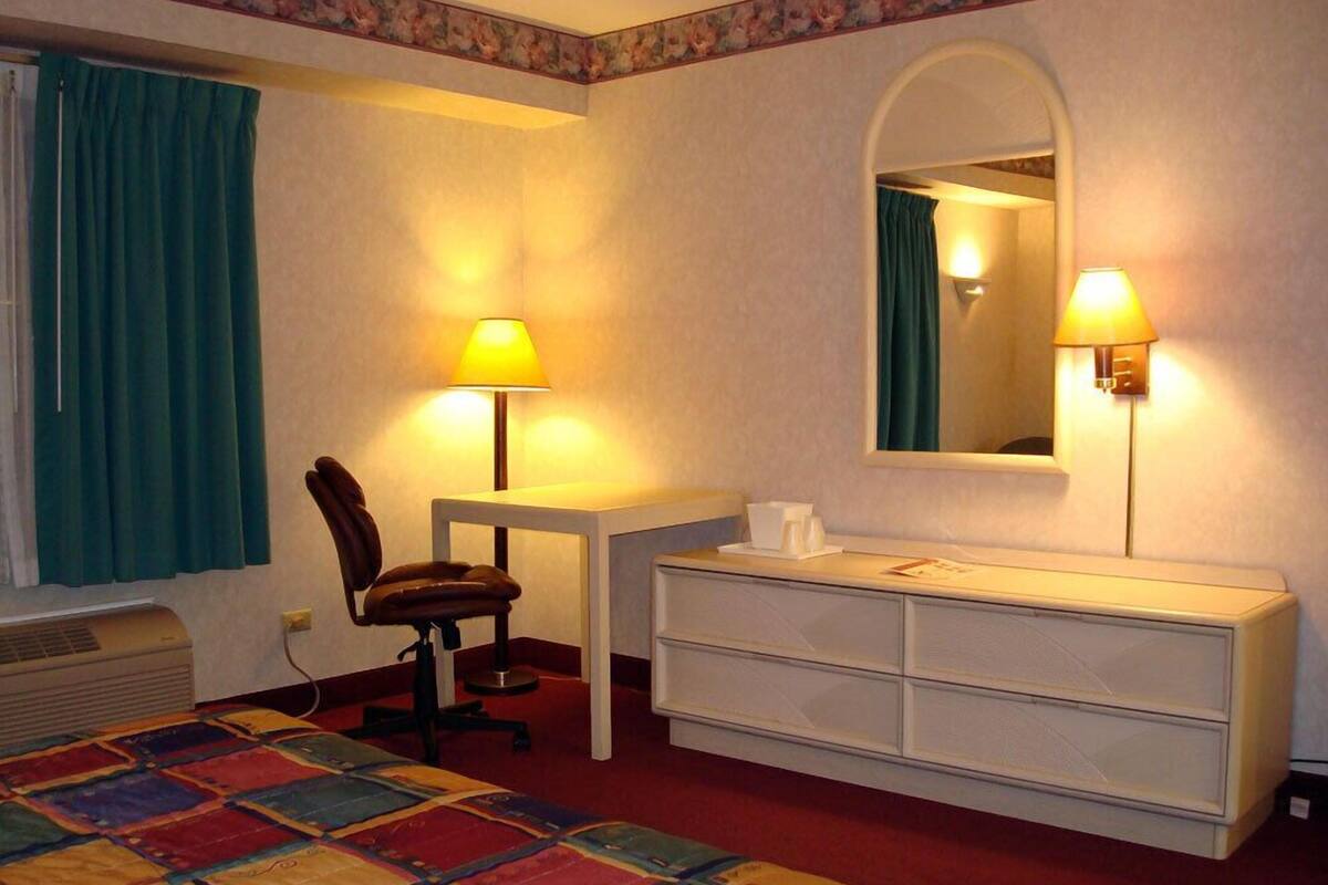 A hotel room with a bed, desk, chair, dresser, and two lamps.