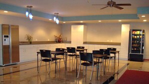 A modern kitchen with a refrigerator, sink, and dining area with chairs and tables. - O'Hare Inn & Suites (Schiller Park)