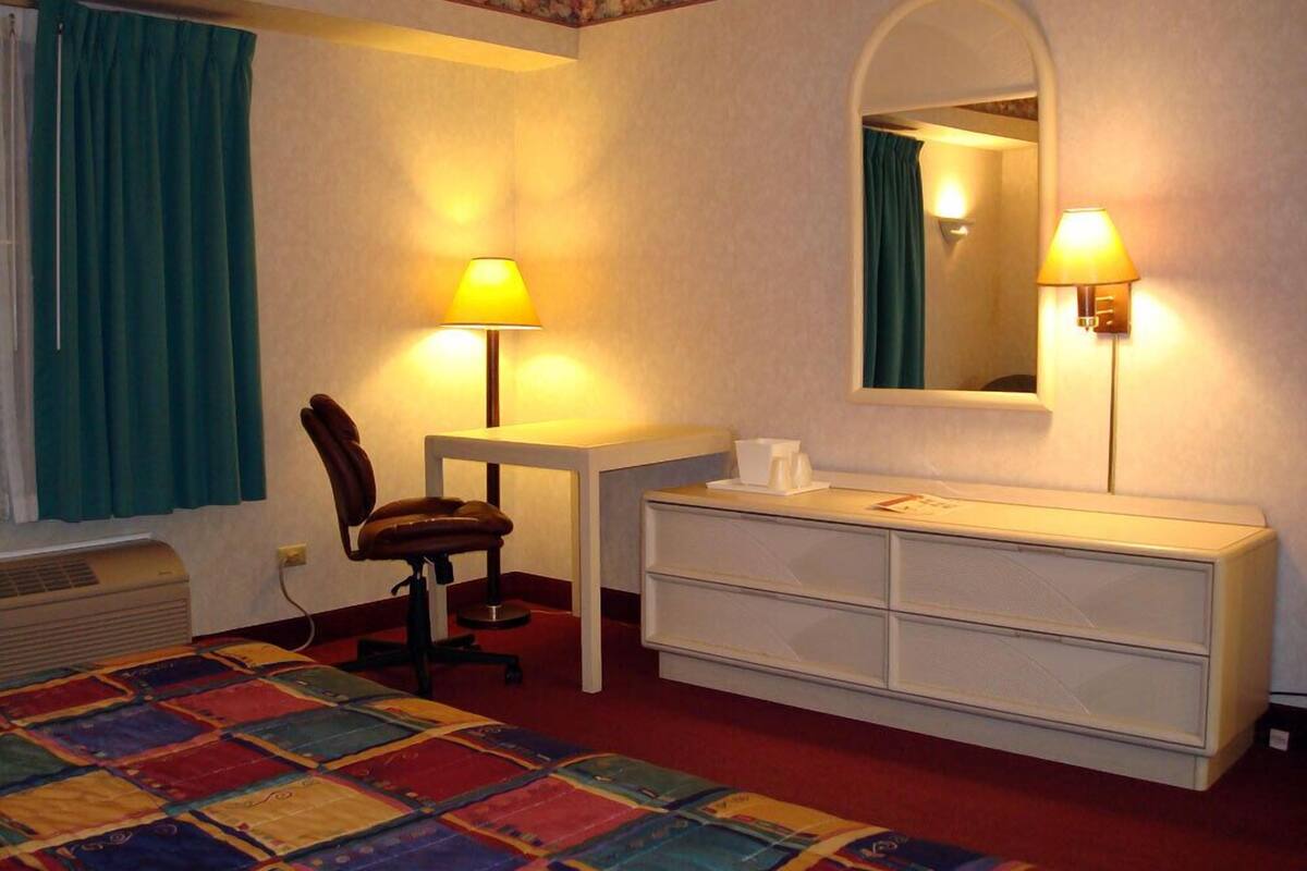 A hotel room with a bed, a desk, a chair, a dresser, and two wall-mounted lamps.