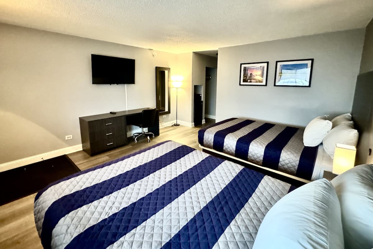 A bedroom with a large bed, a smaller bed, a dresser, a desk, a chair, a TV, and two framed pictures on the wall.