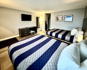 A bedroom with a large bed, a smaller bed, a dresser, a desk, a chair, a TV, and two framed pictures on the wall. - O'Hare Inn & Suites (Schiller Park)
