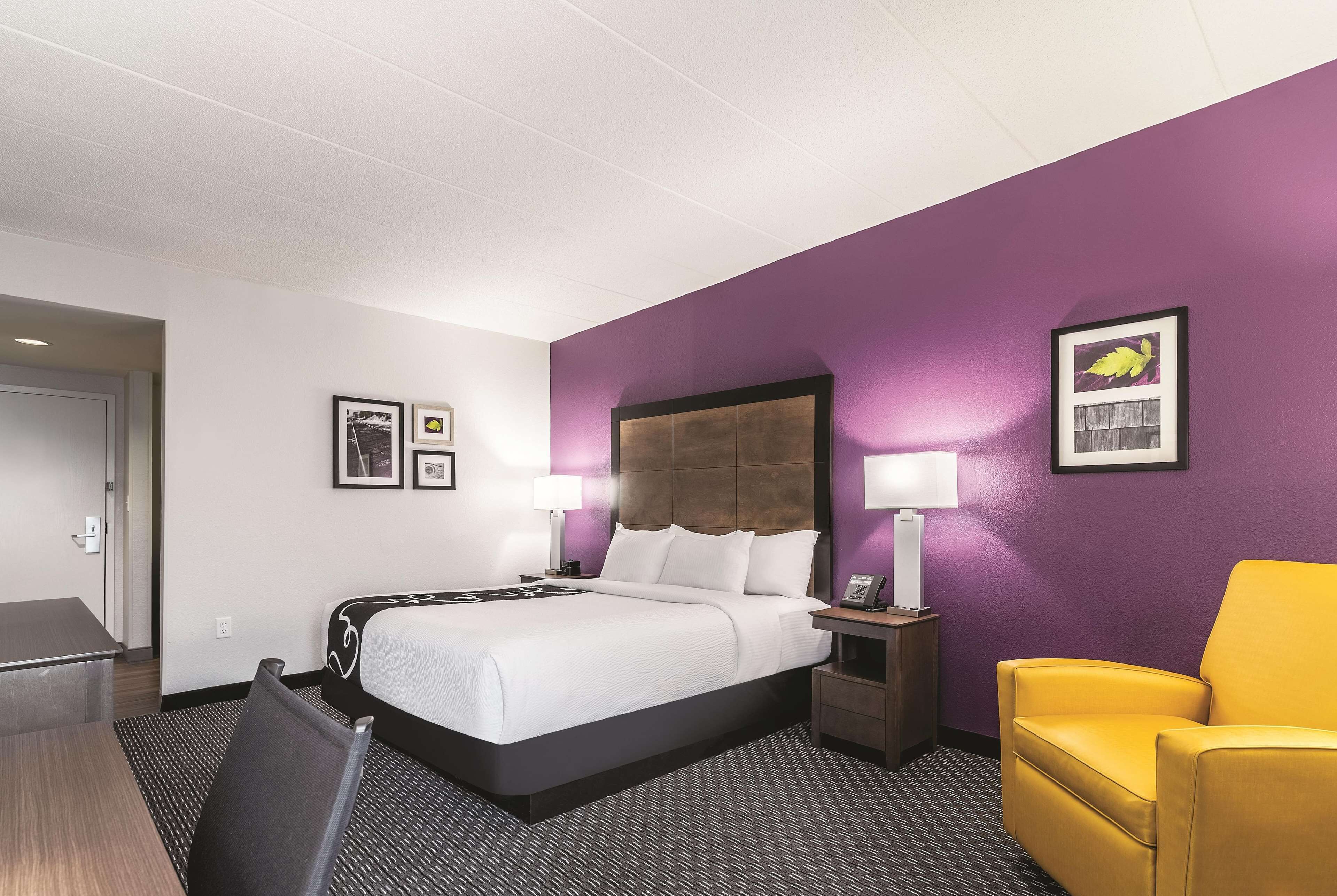 A hotel room with a bed, a desk, a chair, and a nightstand.