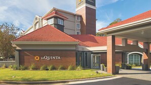 Un hôtel La Quinta avec un toit recouvert de tuiles rouges, une tour imposante et une pelouse bien entretenue.