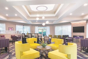 Un hall de hotel con sillones amarillos, una mesa redonda con un florero y un televisor de pantalla plana montado en la pared.