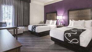 Une chambre d’hôtel avec deux lits, un bureau et une fenêtre avec des rideaux.