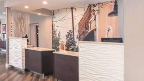 Un espace d’accueil au design moderne, comprenant un comptoir de réception, un écran mural affichant une vue panoramique de la ville et un plancher en bois.
