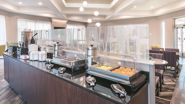 Un espace buffet avec différents stands de nourriture, une machine à café et des tables et chaises.