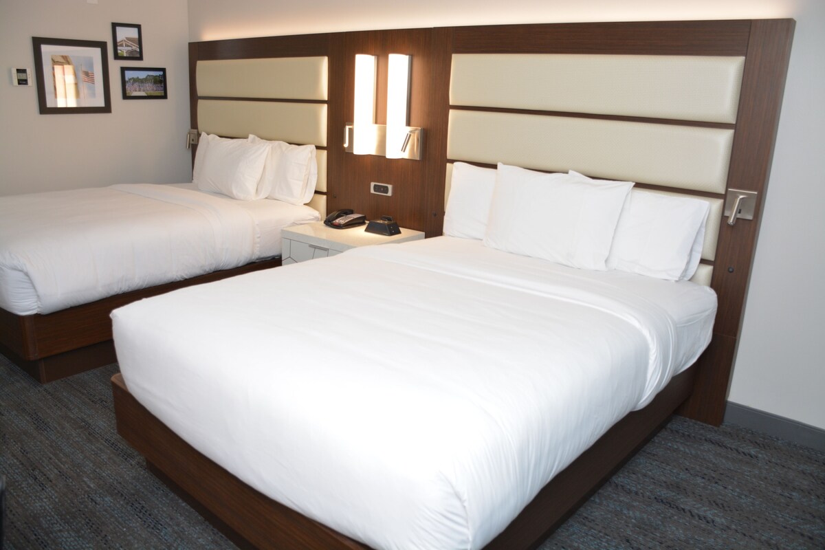 A hotel room with two beds, a nightstand, and a wall-mounted lamp.