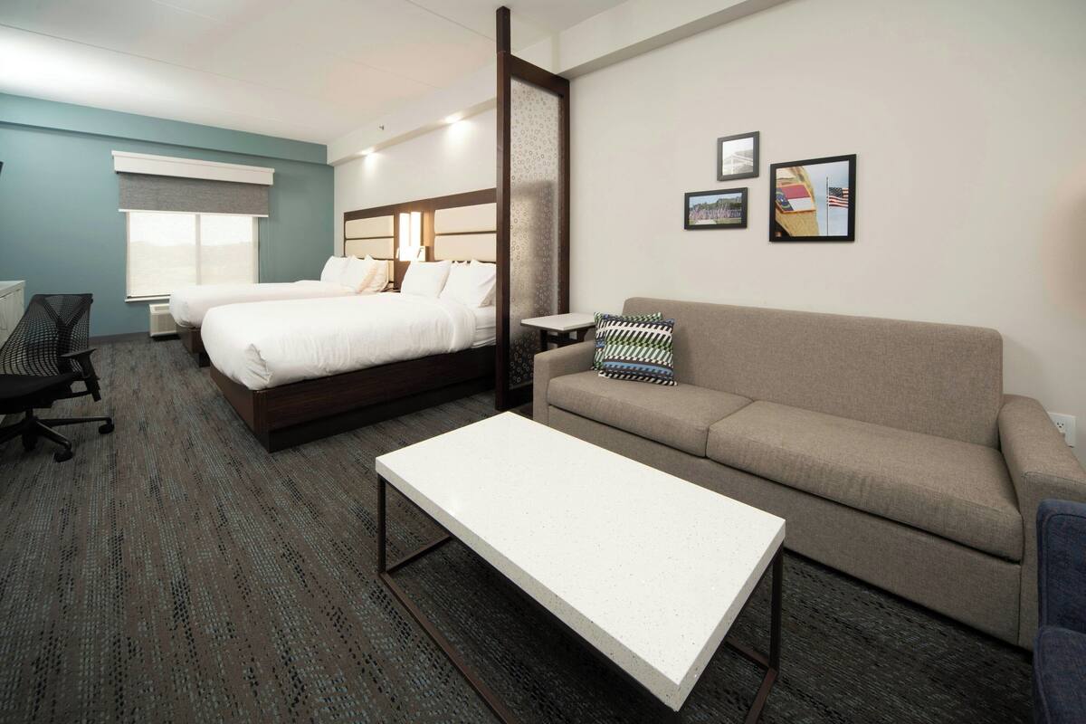A hotel room with two beds, a sofa, a coffee table, and a desk.